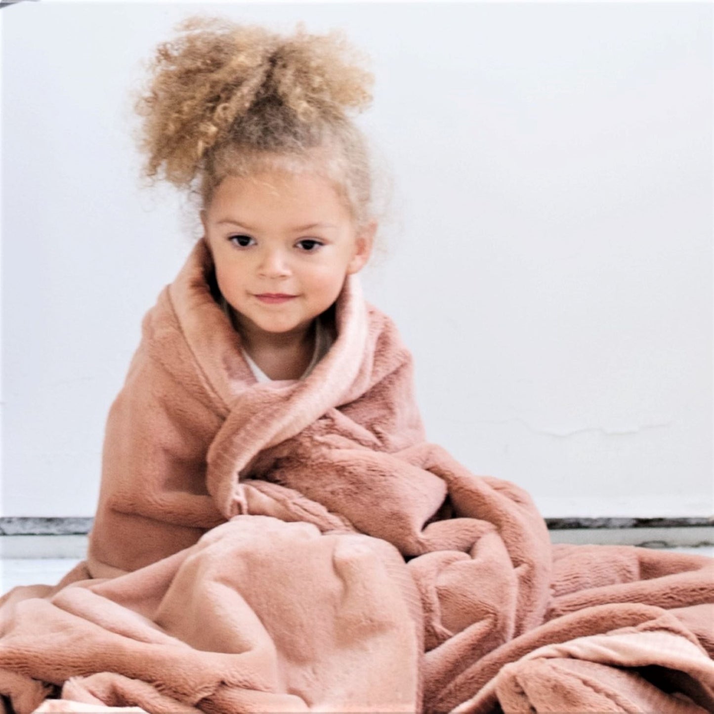 A little girl is wrapped in a Luxury Receiving Rosy (dusty peach) Colored Lush Saranoni Blanket. The soft blanket is a small blanket and a baby blanket or toddler blanket.