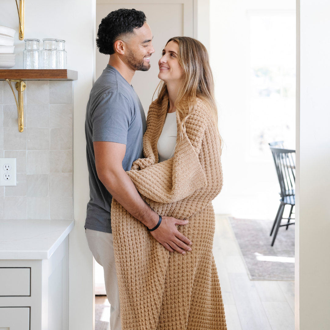 A husband and wife stand with an allspice colored waffle knit blanket. The soft blanket is a Saranoni blanket and a luxury blanket.