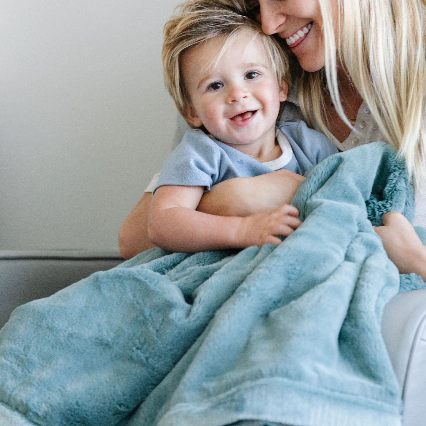 A mother holds her little boy in a Luxury Receiving Dew (light blue) Colored Lush Saranoni Blanket. The soft blanket is a small blanket and a baby blanket or toddler blanket.
