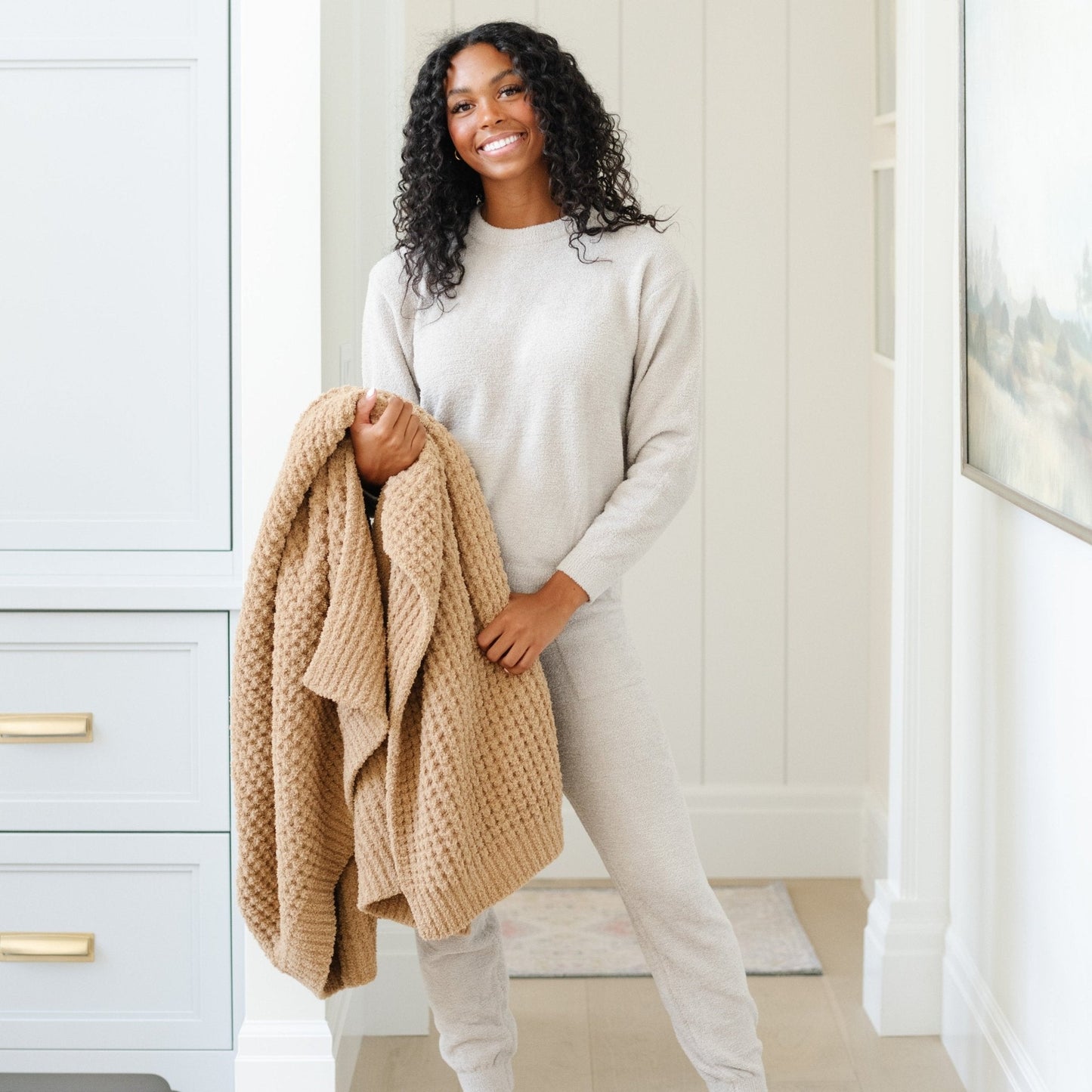 Woman holding a gently draped, cozy, luxurious, waffle knit blanket.