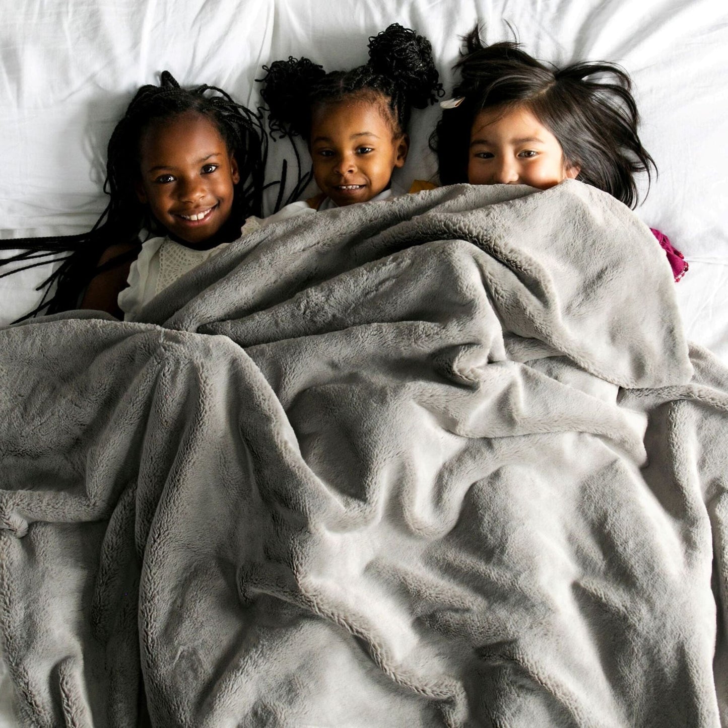 Big fluffy blanket spread out on a bed with kids cuddling underneath.