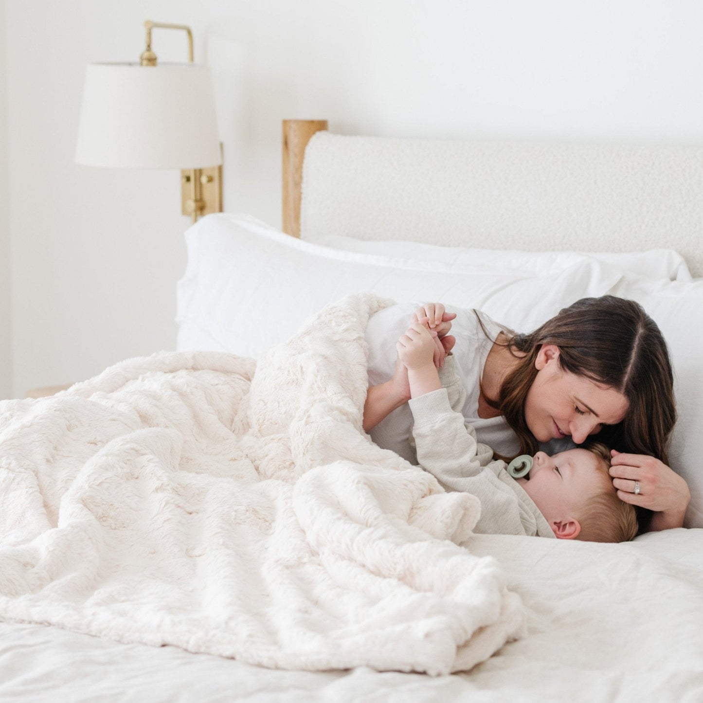 PATTERNED FAUX FUR THROW BLANKETS - Mom and son snuggling underneath a throw blanket on a bed.