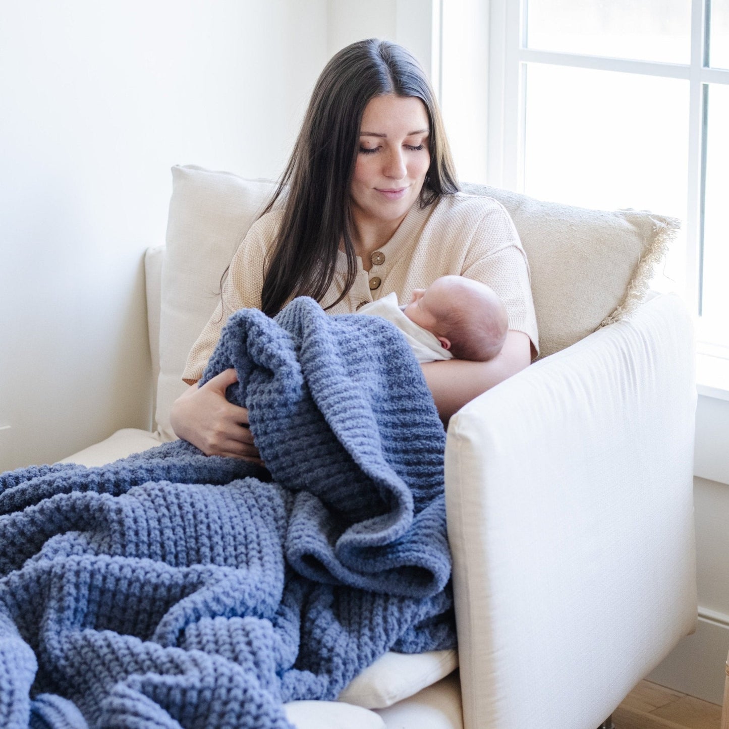 Mother snuggling up with baby, wrapped in blue waffle knit blanket.