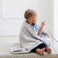 A little boy wrapped in a Luxury Receiving Feather (light gray) Colored Lush Saranoni Blanket. The soft blanket is a small blanket and a baby blanket or toddler blanket.