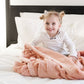 A little girl sits under a Luxury Receiving Blossom (light peachy pink) Colored Lush Saranoni Blanket. The soft blanket is a small blanket and a baby blanket or toddler blanket.
