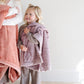 A little girl holds a Luxury Receiving Bloom (dusty purple) Colored Lush Saranoni Blanket. The soft blanket is a small blanket and a baby blanket or toddler blanket.