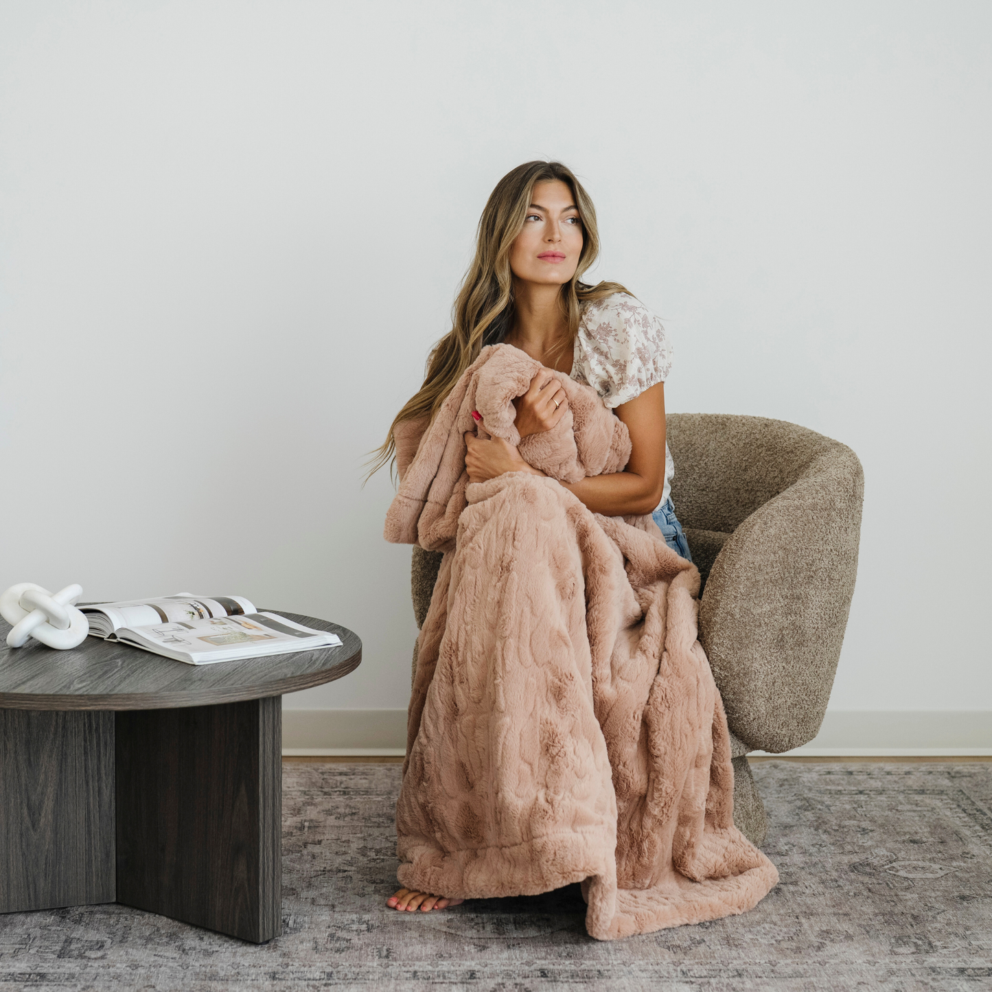 Woman snuggled in chair with a pink faux fur throw cozy blanket. 
