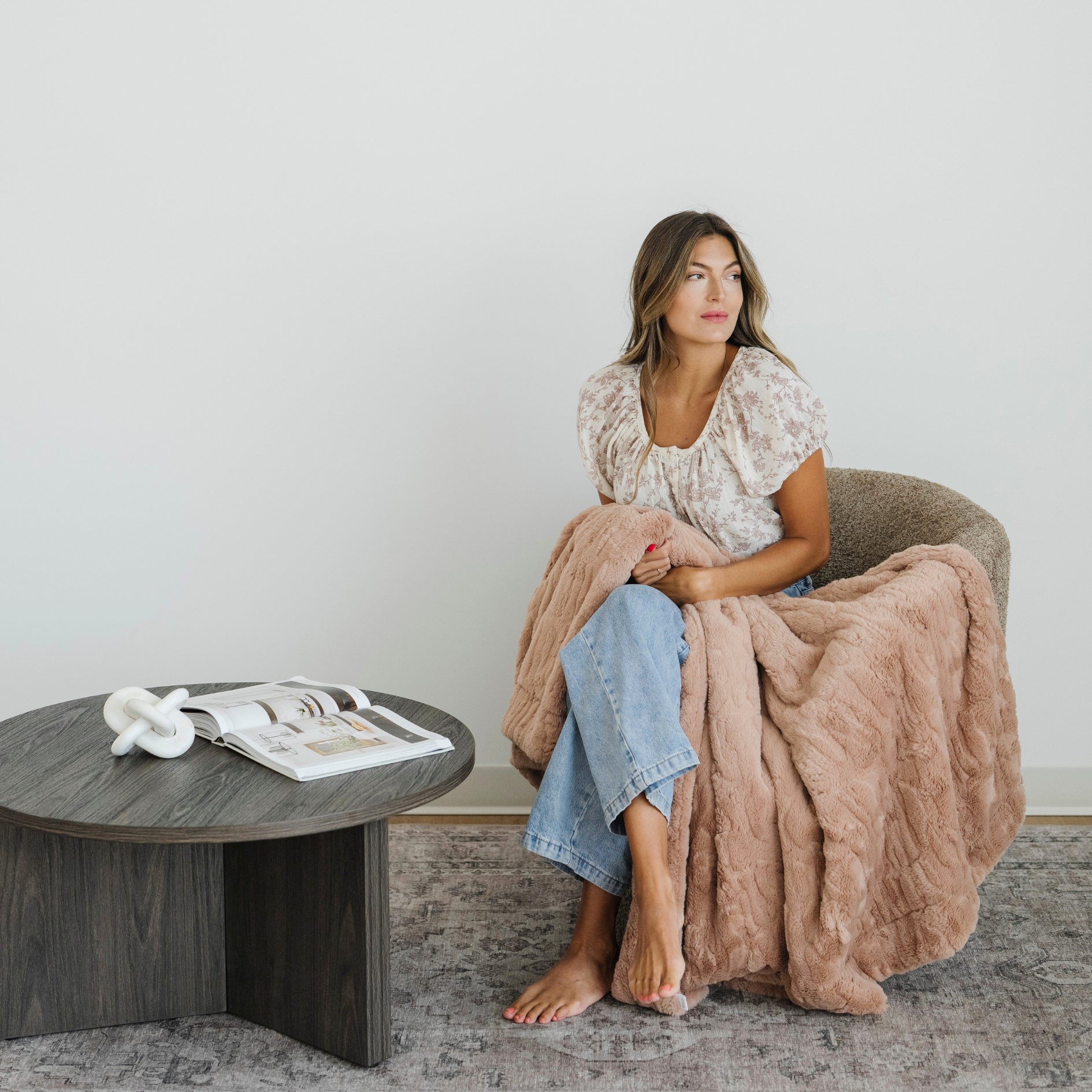 Woman sitting in a chair with a pink faux fur xl throw blanket draped over her. 