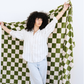 Woman stands with a Minky Stretch olive checkered throw blanket stretched out behind her. 