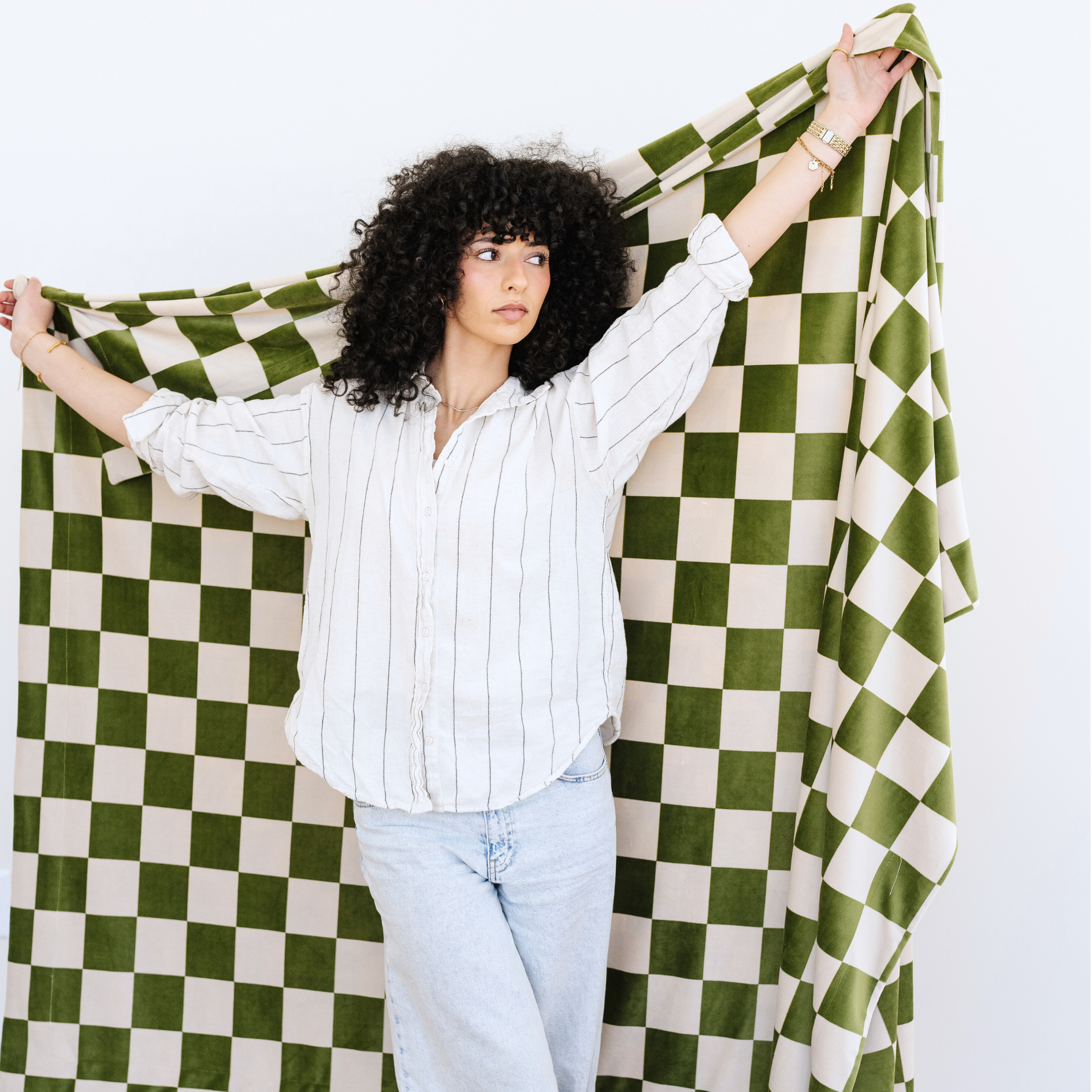 Woman stands with a Minky Stretch olive checkered throw blanket stretched out behind her. 