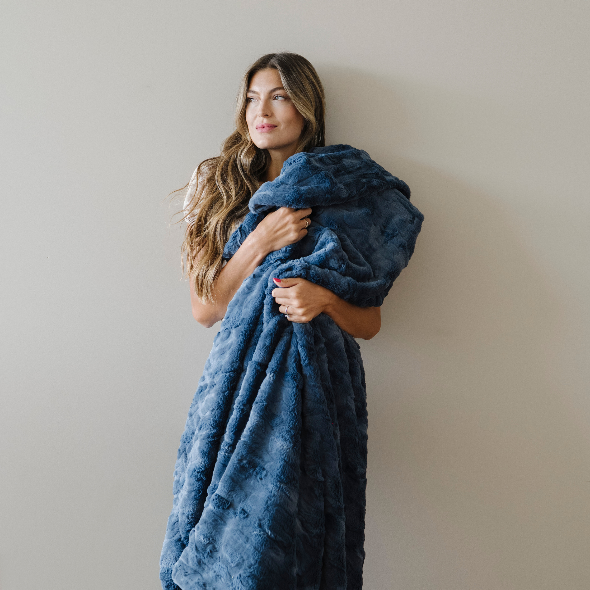 Woman stands holding a indigo blue faux fur cozy blanket in XL size. 
