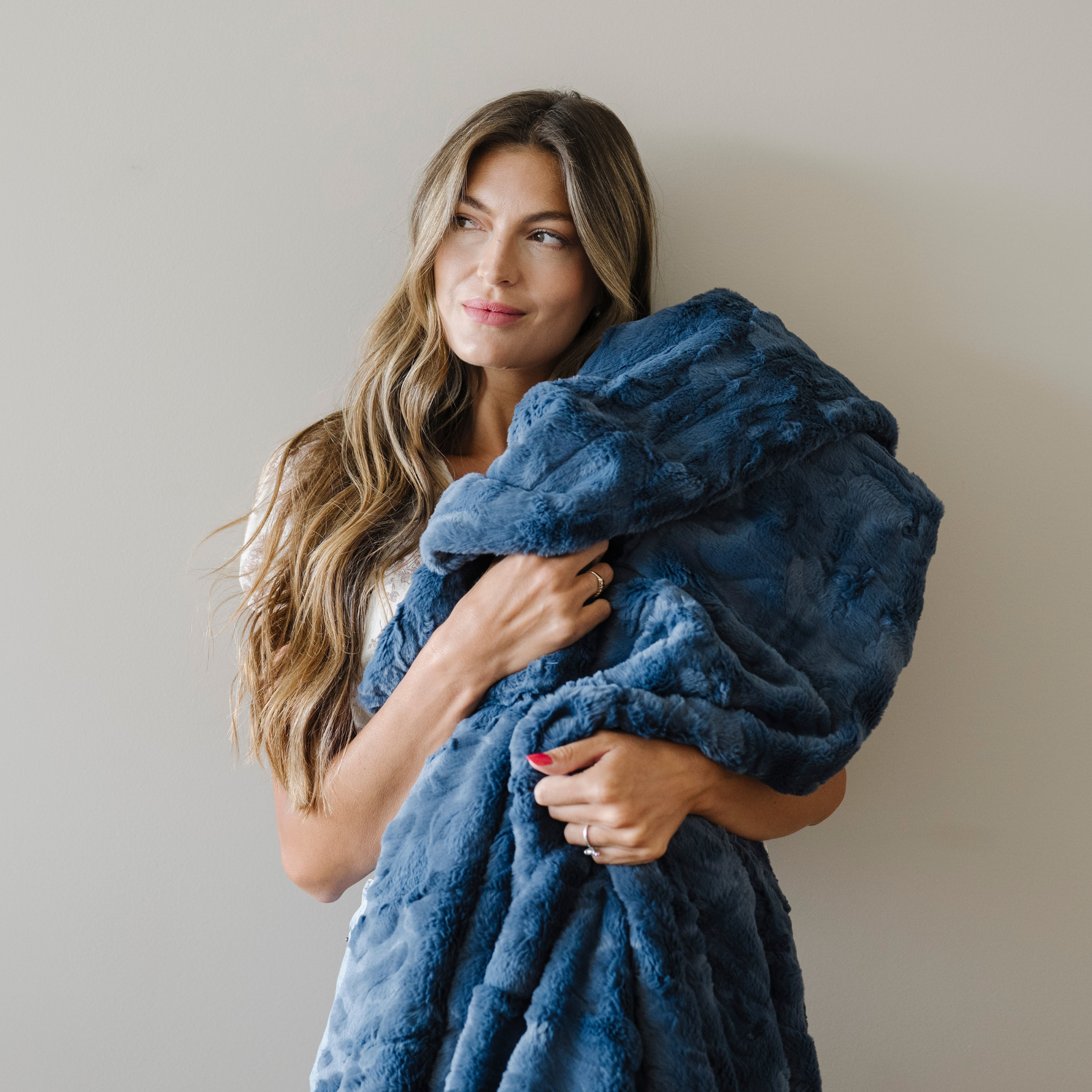 Woman holds a blue faux fur cozy blanket close to her. 