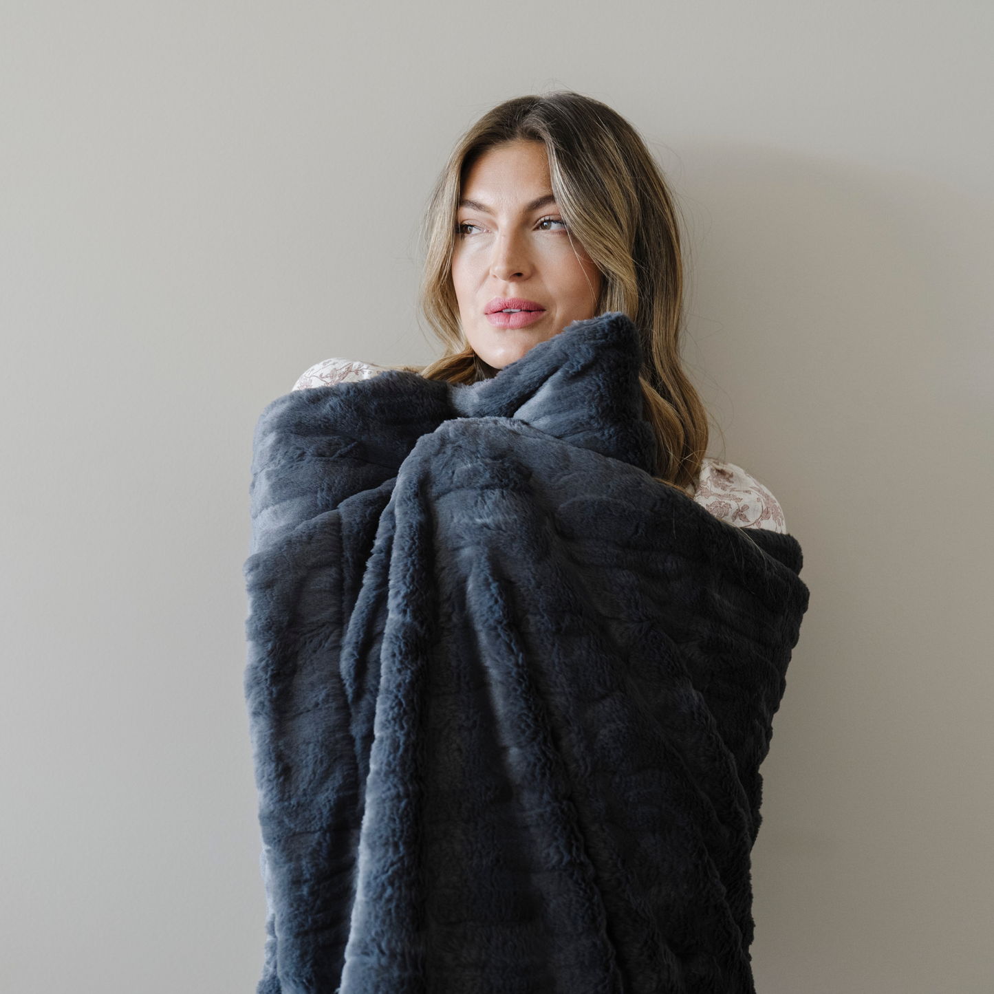 Woman wrapped in a charcoal gray patterned faux fur soft cozy blanket. 