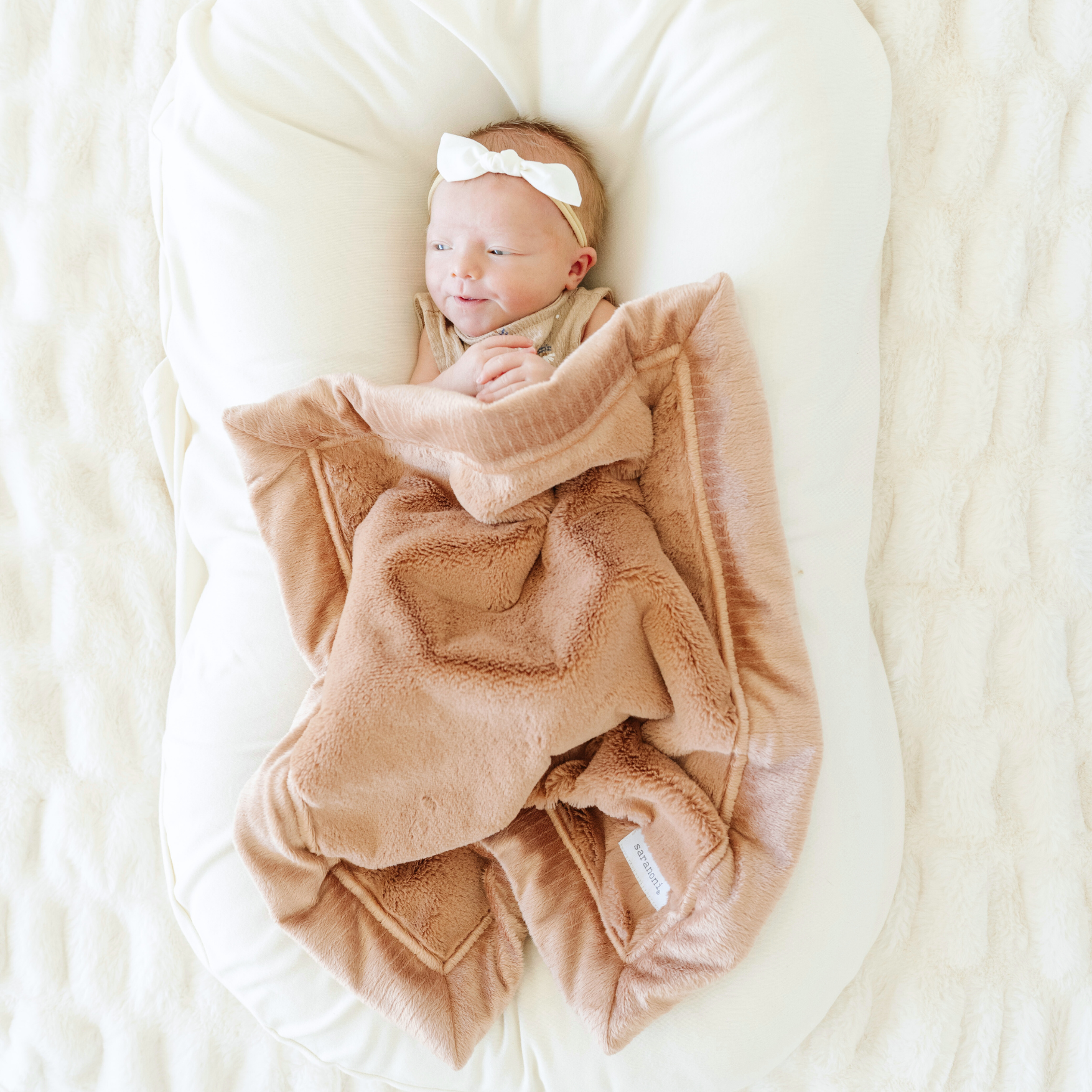Baby girl snuggled with Saranoni Lush Mini baby blanket in Rosy color.