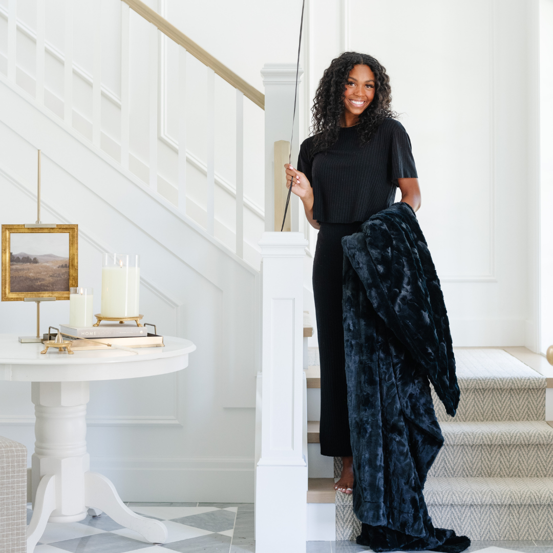 A woman smiles and holds a black luxurious patterned faux fur throw blanket that is a Saranoni blanket. This ultra-soft, plush throw blanket adds a touch of elegance and warmth to any space, perfect as a soft throw blanket or fluffy blanket for lounging. Ideal for those seeking a high-quality artificial fur blanket or luxury blanket, this versatile and stylish soft blanket enhances both comfort and decor. Shop the best blankets and throws for ultimate relaxation and cozy vibes.