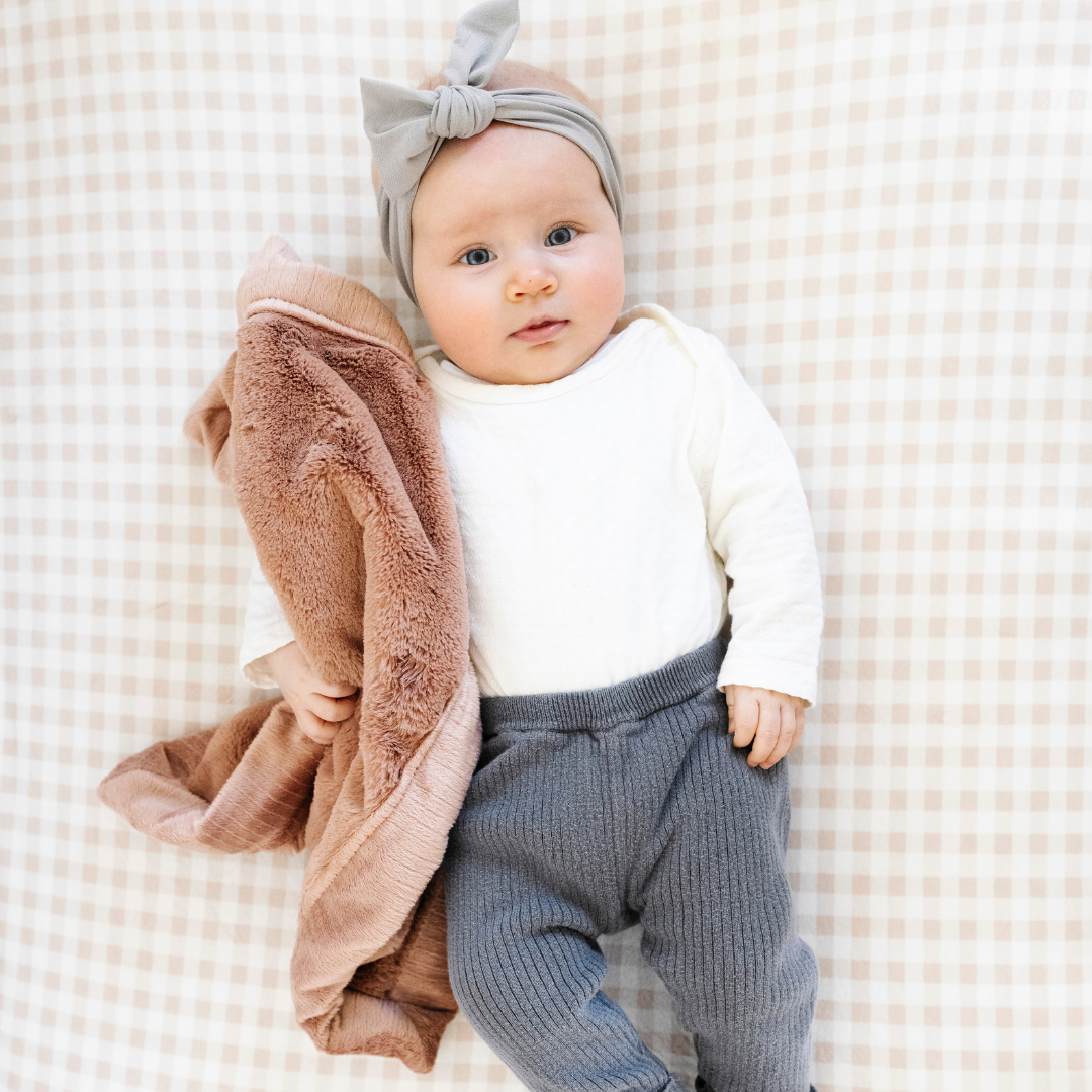 A baby girl and a mini blanket that is a dusty peach colored blanket. The soft blanket is a lush blanket and a baby blanket as well as a Saranoni blanket. This cozy blanket is a luxury blanket for babies and is so soft.