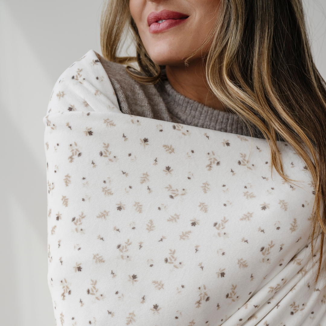 A woman is wrapped in a floral patterned minky stretch throw blanket. This Saranoni blanket is very stretchy, durable, and breathable. This soft blanket is a perfect comfort gift, lounge blanket, or on the go blanket. Enjoy this luxury blanket for years to come. 