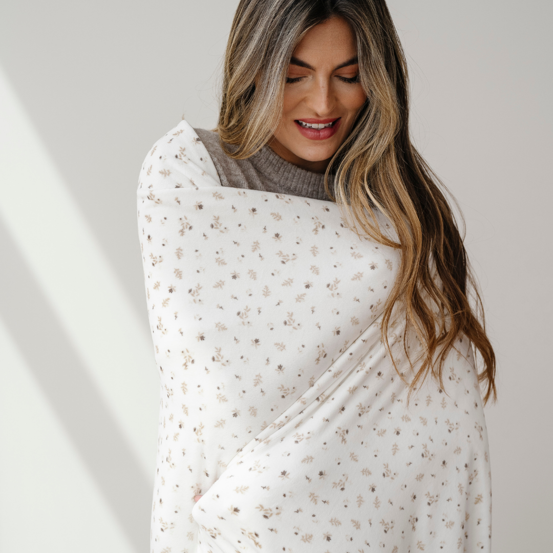 A woman is wrapped in a floral patterned minky stretch throw blanket. This Saranoni blanket is perfect for gifting, lounging, and taking on the go. This soft blanket is also very stretchy and durable. 