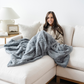 A woman sits on a couch with a blue patterned faux fur blanket. This throw blanket is a great addition to a luxury bedroom or cozy living room. This Saranoni luxury blanket is made to last. 