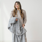 A woman holds a gray blanket that is a patterned faux fur blanket. This blanket has a luxurious texture and is a Saranoni blanket. This luxury blanket can be used for home decor, relaxing, or gifting.  