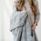 A gray patterned faux fur blanket that is a throw blanket. This cozy blanket is being held by a woman. This blanket makes a great comfort gift, relaxation blanket, or home decor piece. Enjoy this Saranoni blanket for years to come!