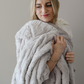 A woman holds a light gray patterned faux fur blanket that is a Saranoni blanket. This throw blanket is luxuriously soft and is great for gifting, relaxing, and using for home decor. This blanket is also very durable and cozy. 