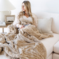 A woman is sitting on a couch with a khaki patterned faux fur blanket. This Saranoni blanket has a luxurious texture and is a throw blanket. Elevate your living room or bedroom with this cozy throw blanket. 