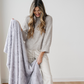 A smiling woman is holding a light gray patterned faux fur blanket. This luxurious blanket adds a touch of elegance to any home and is also great for gifting and relaxing. Enjoy this soft blanket that is a Saranoni blanket. 
