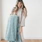 A woman holds a plush throw blanket that is a eucalyptus patterned faux fur blanket. This luxurious blanket elevates a cozy bedroom. This Saranoni blanket is a soft blanket and oh-so cozy. 