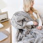 A woman is holding a plush cashmere colored patterned faux fur blanket. This Saranoni blanket has a luxurious texture and elevates every space. Use this throw blanket as a comfort gift, relaxation blanket, or home decor staple.