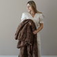 A woman holds a brown patterned faux fur blanket. This soft blanket is a Saranoni blanket with a very luxurious texture. Add to your luxury living with this blanket and also use it for home decor. 