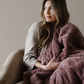 A woman holds a dusty mauve patterned faux fur blanket. This luxury blanket is perfect as a gift, for relaxing, or for a luxury aesthetic. This throw blanket is durable and also a Saranoni luxury blanket. 