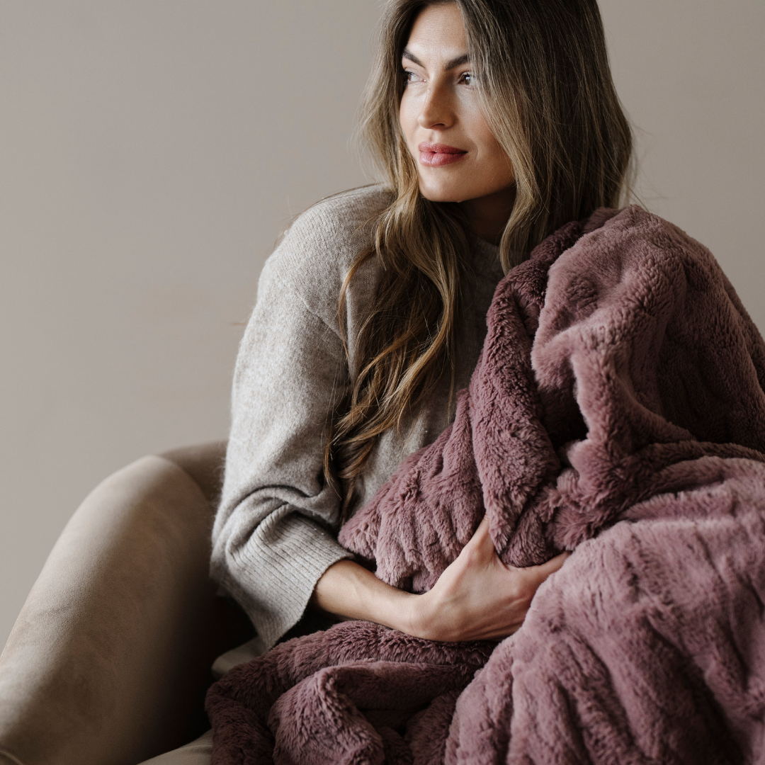 A woman holds a dusty mauve patterned faux fur blanket. This luxury blanket is perfect as a gift, for relaxing, or for a luxury aesthetic. This throw blanket is durable and also a Saranoni luxury blanket. 