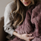 A woman sits on a chair and is holding a dusty mauve Saranoni blanket. This soft blanket is a luxury blanket and a patterned faux fur blanket. The luxurious texture of this blanket makes it perfect for gifting, relaxing, or using for home decor. 