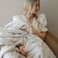 A woman holds a light tan patterned faux fur blanket. This soft blanket is a Saranoni blanket. This luxury throw is perfect for gifting, lounging or home decor. It's luxurious texture makes it an extra cozy blanket. 