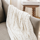 A floral patterned minky stretch blanket is draped on a chair. This throw blanket is a Saranoni blanket and is great for gifting, loungewear, and taking on the go. Enjoy this soft blanket for years to come. 