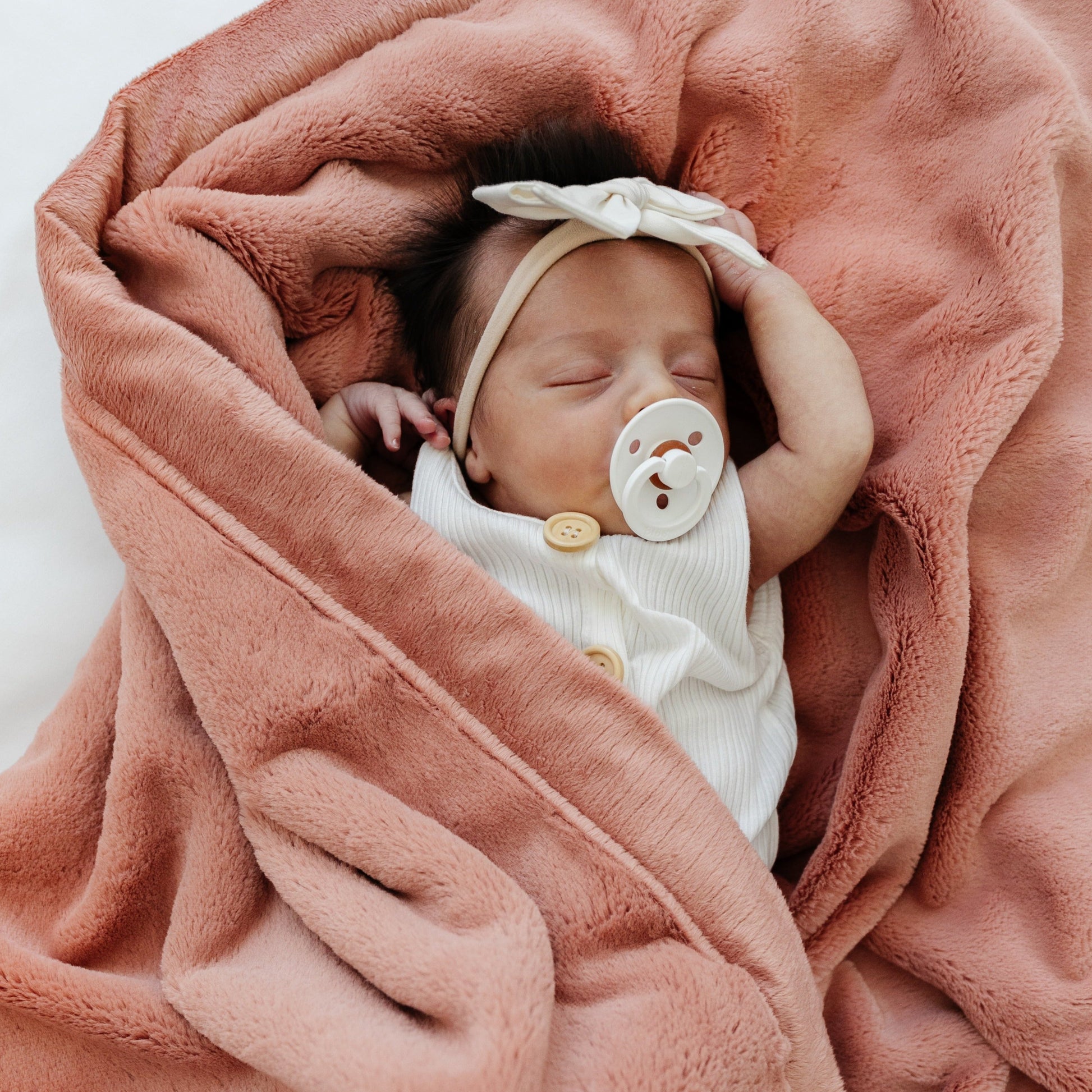 A baby girl lays in a Luxury Receiving Clay Colored Lush Saranoni Blanket. The soft blanket is a small blanket and a baby blanket or toddler blanket.