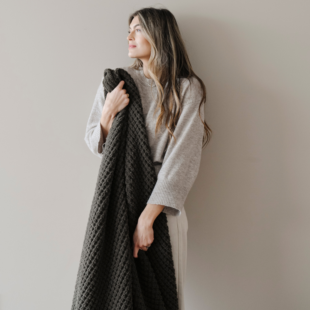 A woman holds a green waffle knit blanket. This soft blanket is a Saranoni blanket and is also very stretchy and breathable. Enjoy this throw blanket for relaxing, gifting, or as home decor. 