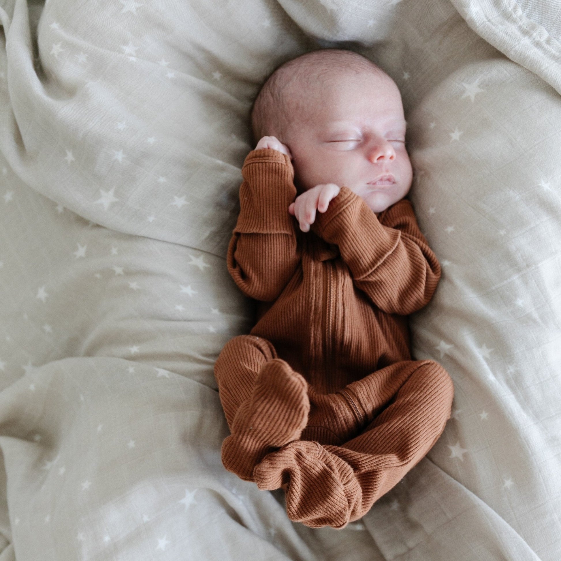 Newborn baby laying on a taupe star print bamboo swaddle.