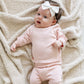 A baby girl lays on a Saranoni Blanket. She is wearing a light pink, 100% cotton Saranoni baby outfit that combines style and comfort. The Saranoni cloud-soft cotton set features a breathable waistband, loosely fitted sleeves, and elevated button details, making it perfect for everyday wear or special occasions. This heirloom-quality baby clothing offers timeless style and ultimate comfort. Ideal for parents searching for luxury baby clothes, soft cotton baby sets, or high-quality infant outfit.