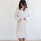 Woman in a light gray waffle knit robe, standing in a bright room.