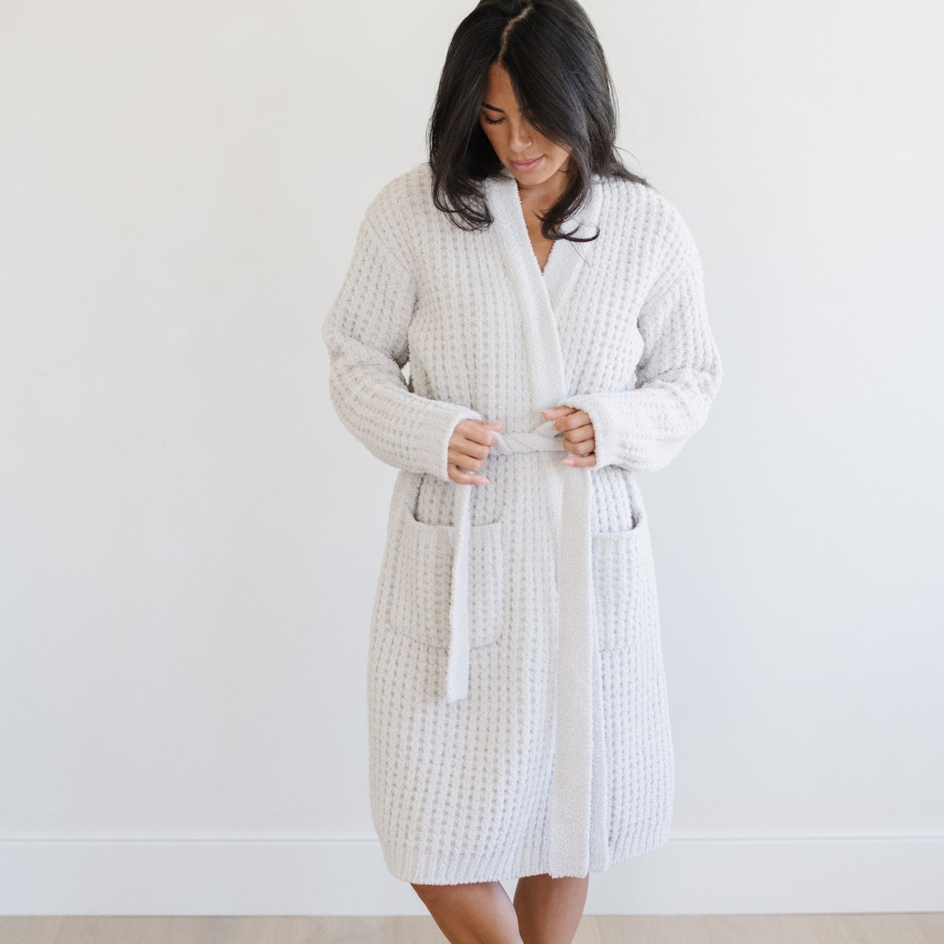 Woman in a light gray waffle knit robe, standing in a bright room.