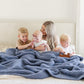 Mom and kids laying with blue waffle knit blanket. 